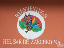 The colorful hand-painted signe reads, "Bienvenidos Helsar de Zarcero SA", with an image of a butterfly on a coffee tree.