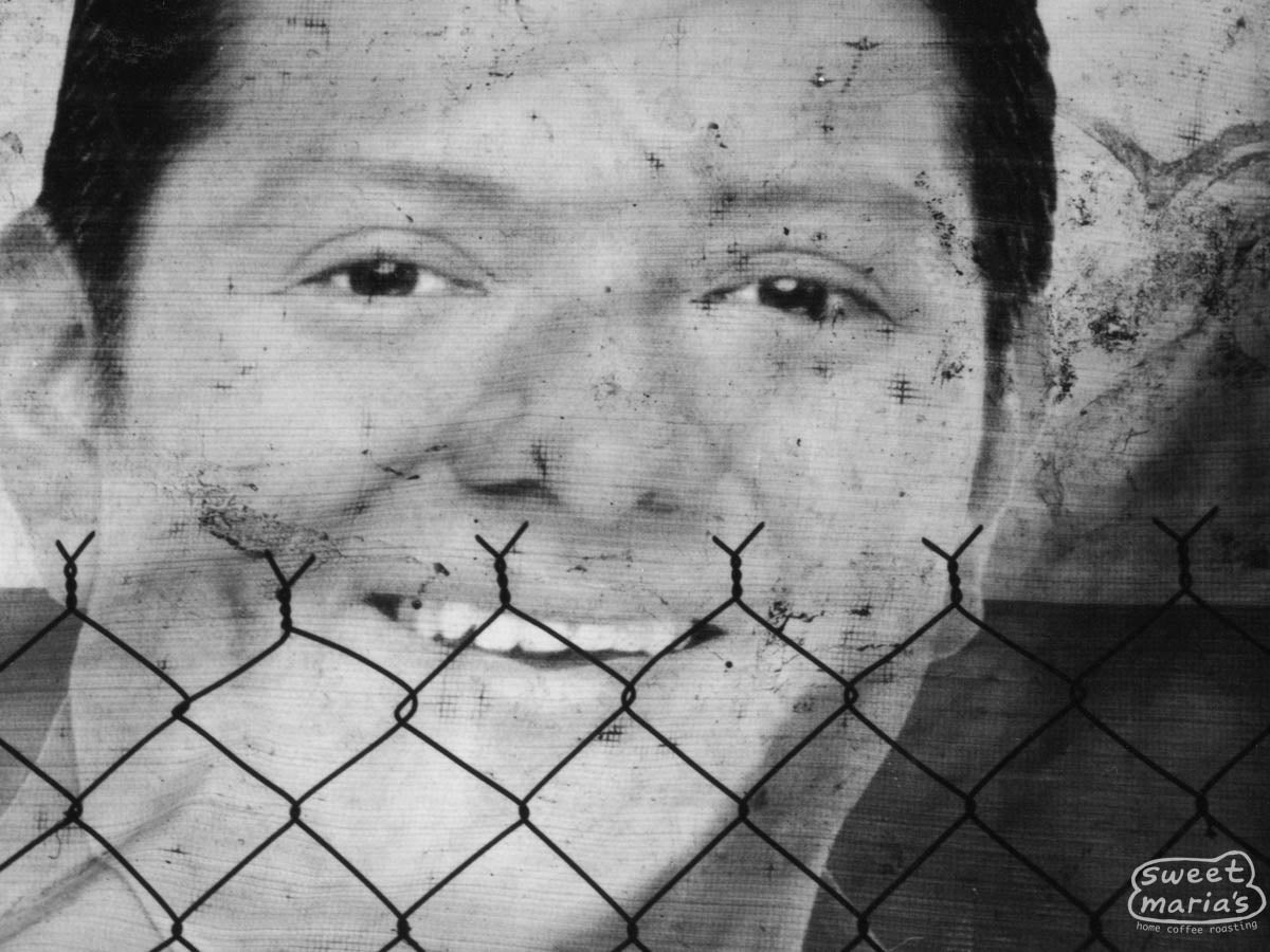 Mural of a man's smiling face behind a chain link fence in Chiapas.