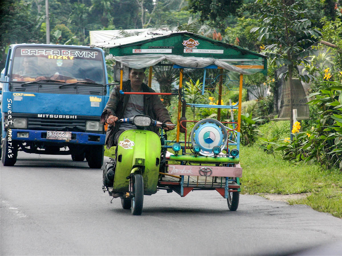 A tuk tuk driver and his green scooter putting down the streets of Central Aceh.