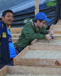 Raul Hector Trujillo (left) stands next to his drying coffee while Pedro (right) snaps photos.